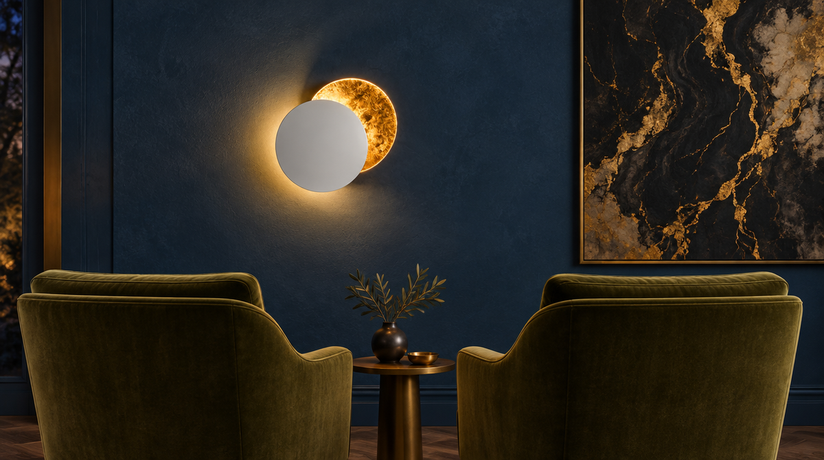 Arandela Eclipse Nórdica branca com dourado acesa em parede azul entre duas poltronas de veludo